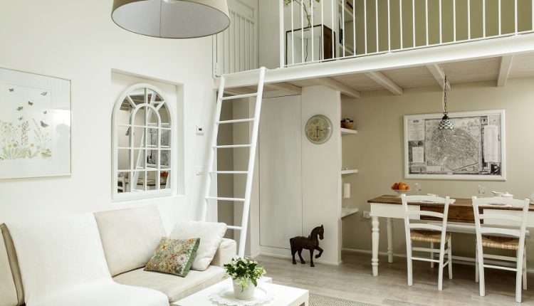 Bright white living room with a cream sofa, white coffee table, ladder to a loft, and a dining area with a large map on the wall.