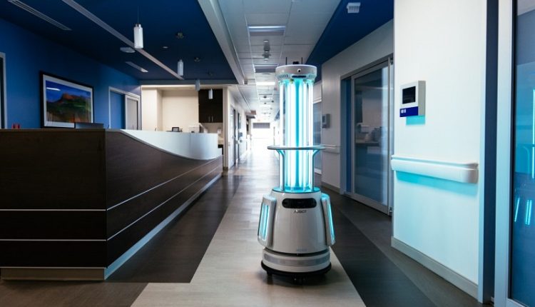 Hospital corridor with a tall autonomous UV sterilization robot glowing blue in the center of the hallway.